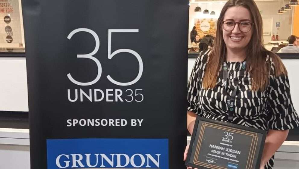 Reuse Network Commercial Manager Hannah Jordan with her 35-under-35 award, standing next to a RWM pop-up banner promoting the awards
